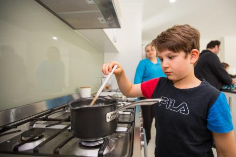 A young boy cooks his dinner while his parents supervise.